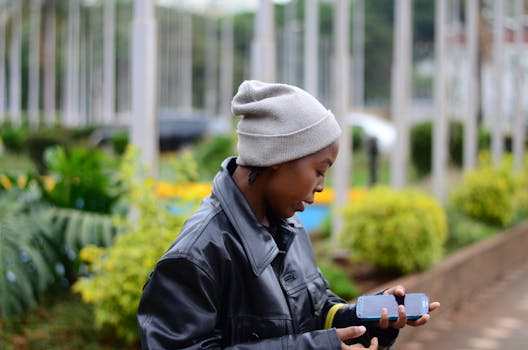 Young woman wearing a beanie and leather jacket, using smartphone outdoors in Nairobi.